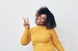 © Carlos David - Studio portrait of cheerful mid aged black woman with curly hairstyle making peace sign with right hand.