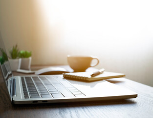 Wall Mural - soft focus of Office desk table with keyboard of laptop computer, coffee cup and notebook, glasses. Business and finance concept. Workplace with morning sunlight from window with copy space.