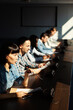 © Comeback Images - Side view of group of multiethnic business people sitting at desk in row taking part in conference with microphones in front of them. Focus on young Asian woman speaking in meeting