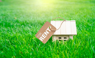 Concept of environmentally friendly home for rent. House built from natural building materials. Little wooden toy house with tag For rent on the green grass.