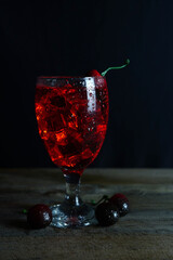 Wall Mural - Vertical shot of an iced cherry cocktail on a table against a black background