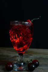 Wall Mural - Vertshot of an iced cherry cocktail on a table against a black background