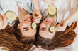 © Daria Lukoiko - Two girls make homemade face and hair beauty masks. Cucumbers for the freshness of the skin around the eyes. Women take care of youthful skin. Girlfriends laugh at home lying on the floor on pillows.