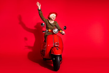 Full length photo of cheerful aged woman happy positive smile ride bike wave hello isolated over red color background