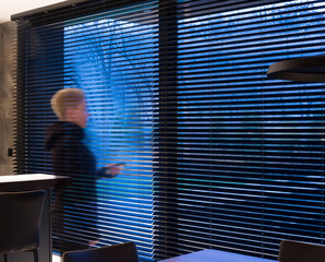 Leinwandbilder - Motorized wood blinds black color in the interior. Automatic venetian blinds closeup on the large windows. The park is visible through the blinds. The girl holds a blinds control panel in her hands.