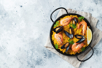 Traditional spanish seafood paella in pan with chickpeas, shrimps, mussels, squid on light grey concrete background. Top view with copy space