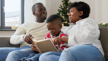 Wall Mural - family, winter holidays and people concept - happy african american mother, father and baby son reading book at home on christmas