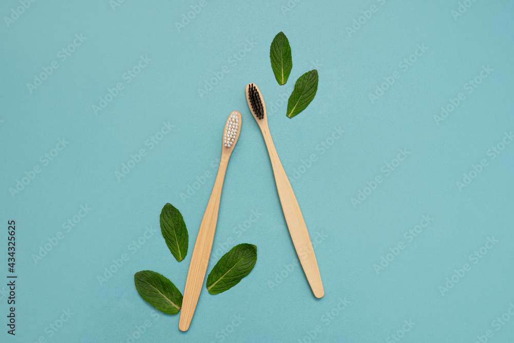 Two wooden bamboo toothbrushes with mint leaves on a blue background ...
