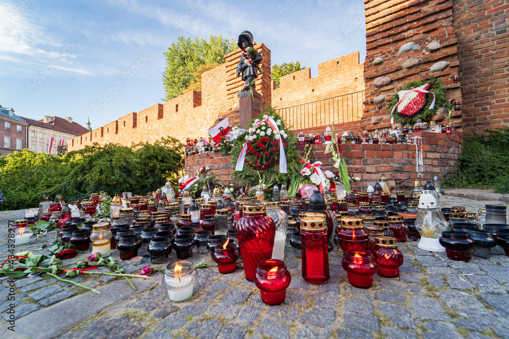 Warsaw Uprising Memorial Day, flowers, candles and Polish flags near Little Insurrectionist sculpture, a statue of the child soldiers. Honoring victims of 1944 revolt - obrazy, fototapety, plakaty 