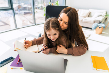 Happy mother and daughter are doing homework while sitting at the laptop