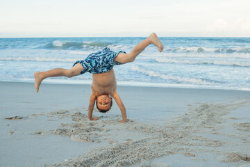 Boy doing a somersault on the sand on the beach. Exciting child having fun on the beach. Vacations by the sea. Outdoor activities with children. Summer swimming.