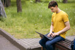 © halcon1 - A student sits on a park bench and uses a laptop. Remote freelance work or outdoor student distance learning. An IT professional works remotely from a laptop. Free space for text