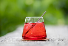 Ice Red Drink In The Glass On Natural Green Bokeh Background.