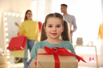 Sticker - Little girl with gift box near her parents in store. Family Christmas shopping