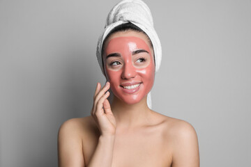 Woman applying pomegranate face mask on grey background