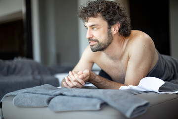 Handsome man lying in a spa salon waiting for back massage and relaxation. Wellness and leisure time for health care together. Focus on the man. Look at the camera.