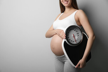 Canvas Print - Pregnant woman with scales on grey background, closeup. Space for text