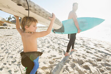 Father And Son Carrying Surfboards To Beach