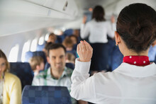 Rear View Of Flight Attendant Indicating Exits To Passengers In Airplane