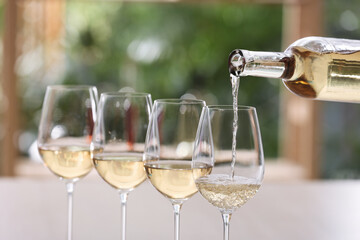 Poster - Pouring white wine from bottle into glass on blurred background