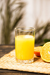 Wall Mural - A glass of fresh orange juice on a straw mat and wooden table.