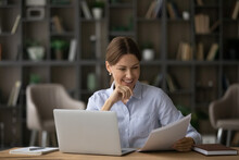 Good Business. Smiling Satisfied Millennial Female Reading Paper Documents Before Computer Screen Plan To Accept Good Commercial Offer Proposal. Happy Young Woman Engaged In Paperwork At Home Office
