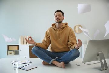 Poster - Calm man meditating on office desk in middle of busy work day