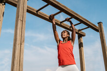 African Young Woman Climbing Monkey Bars In Military Training Boot Camp Outdoors At City Park - Focus On Girl Face