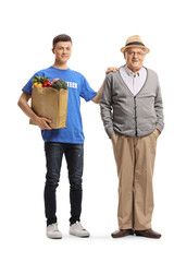 Canvas Print - Young male volunteer holding a grocery bag and standing next to elderly man