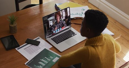 Canvas Print - African american female teacher talking and taking notes while having a video call on laptop at home