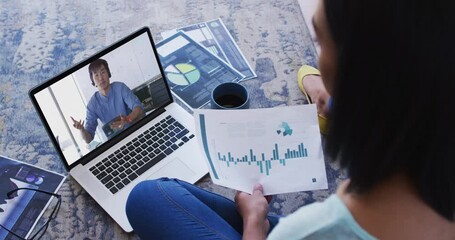 Wall Mural - African american woman holding a document having a video call on laptop at home