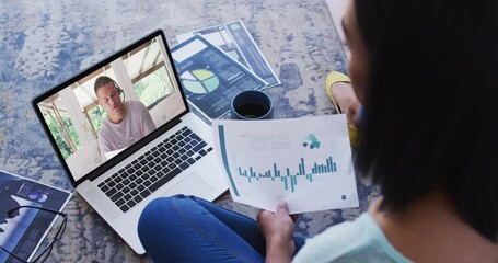 Wall Mural - African american woman holding a document having a video call on laptop at home