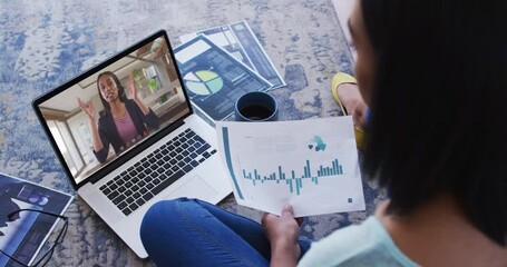 Wall Mural - African american woman holding a document having a video call on laptop at home