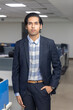 © Bhaven - Portrait of handsome young Indian businessman standing against corporate office background.
