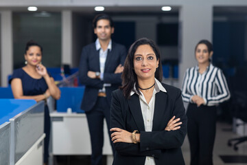 Confident Indian businesswoman standing infront of her office colleagues, selective focus, corporate environment, team members, business office.