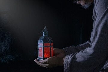 hand of old Muslim man with Arabic lantern on black background, Islamic Ramadan Kareem concept