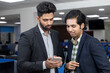© Bhaven - Portrait of two young handsome Indian businessmen looking into phone, discussing project, corporate environment.