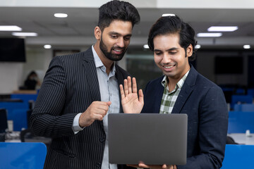 Portrait of two young handsome Indian businessmen looking into phone, discussing project, corporate environment.