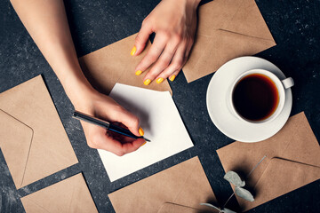 Wall Mural - Woman writes letter on black background top view and envelopes around