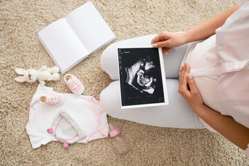 Wall Mural - Pregnant woman with sonogram image and baby accessories on floor