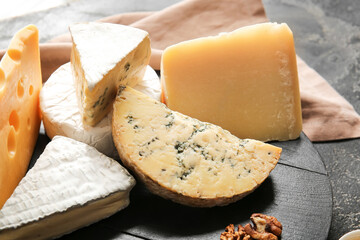 Tray with different types of cheese on dark background, closeup