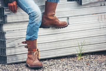 Wall Mural - Men wear construction Boots safety footwear for worker at construction site. Engineer Wear Jeans Brown Boots Worker on Background of Refinery. Engineer safety industry fashion footwear walking outdoor