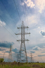 poles of high-voltage power lines, in a field, stretching in perspective against a cloudy sky