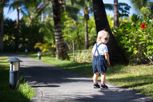 Adorable Fashion Baby Toddler Boy, Dressed In Casual Clothes, Walking In A Beautiful Resort Gardens