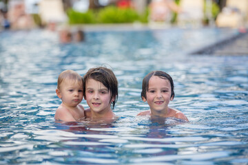 Sticker - Adorable happy little child, toddler boy, having fun relaxing and playing with his older brothers in a pool on sunny day during summer vacation