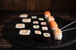 Sushi sind aufgelegt auf der schwarzen Platte, Schwarze Stäbe fassen ein Sushi an. Sehr gut geeignet für chinesischen Restaurant, Asia Küche