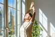 © Nata Bene - Enjoying new day. Beautiful happy mature woman stretching body and smiling while standing with closed eyes in sun rays shining through window on sunny morning at home. Optimism and happiness concept
