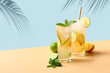 Two Summer Cold Mojito Cocktails With Orange And Lime Slices On Blue And Beige Background. Refreshing Summer Beverage With Sunny Shadow.