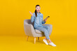 © deagreez - Photo of shiny impressed lady dressed jeans shirt spectacles sitting chair rising arm typing device smiling isolated yellow color background