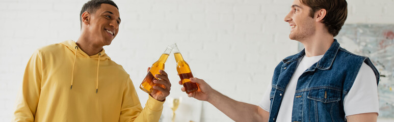 Wall Mural - young smiling interracial friends clinking with bottles of beer, banner